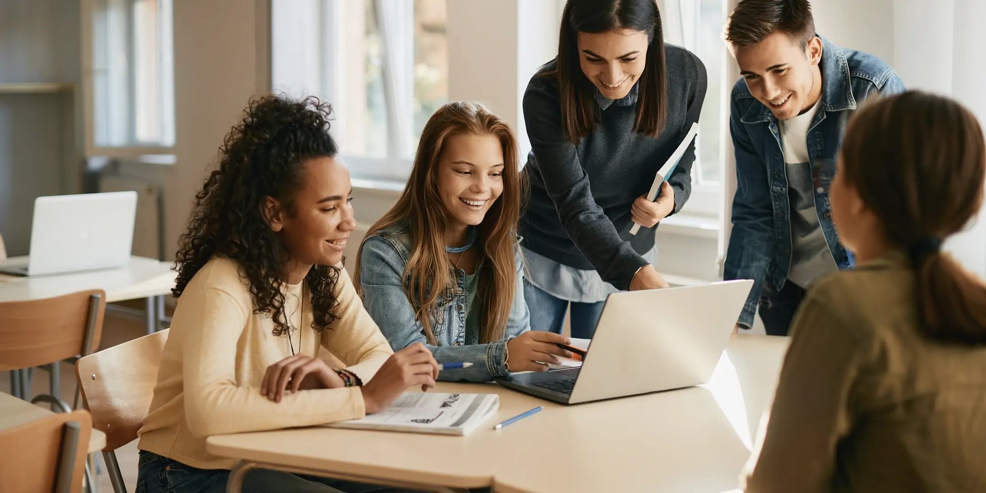 A group of students looking at laptop in a classroom